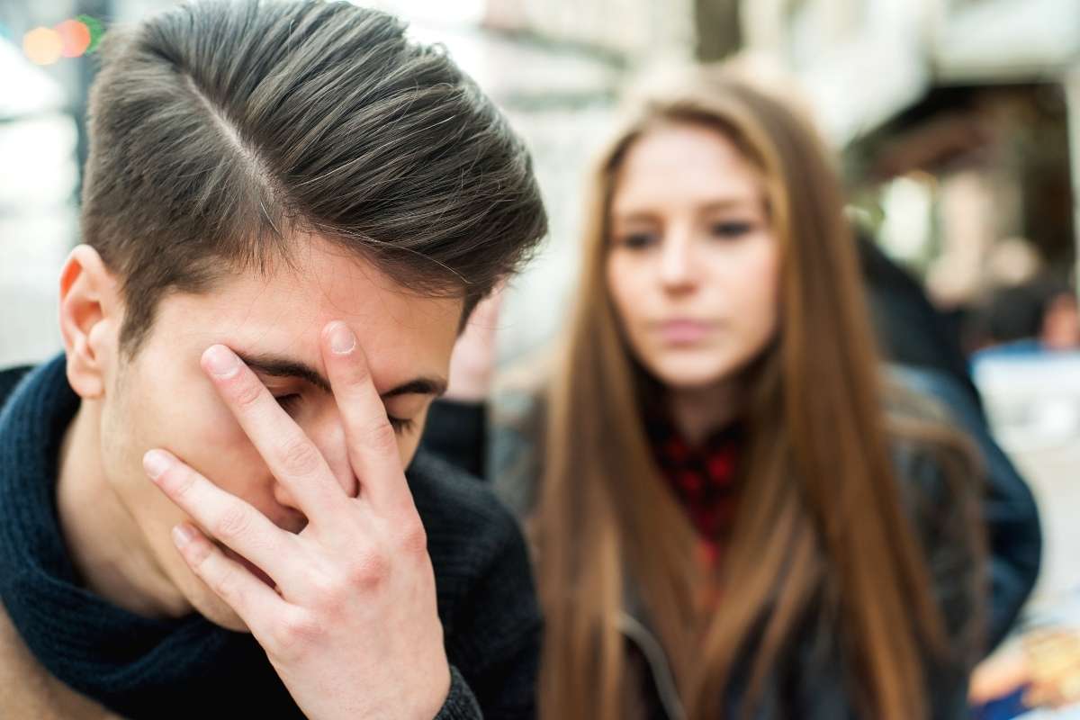 uomo con mano davanti al viso donna dietro