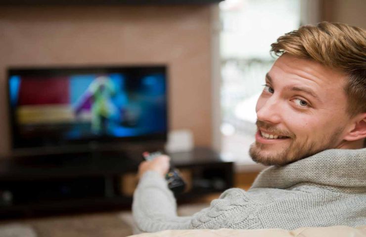 uomo che guarda la tv rivolto verso di noi sorridente